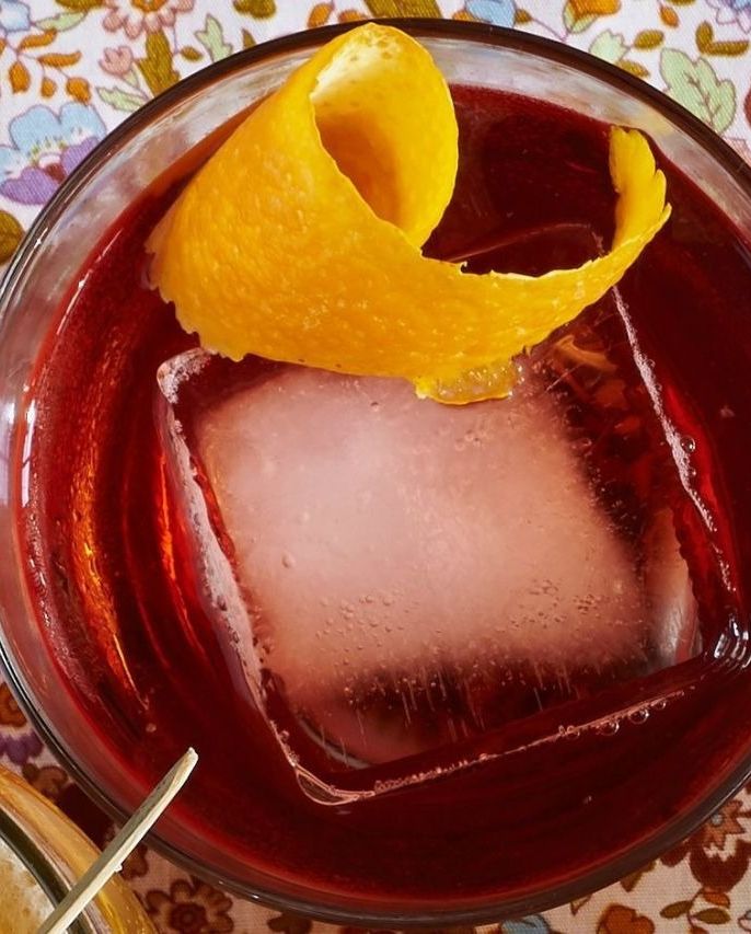 bourbon negroni in a glass with a large square of ice and a curled strip of lemon peel