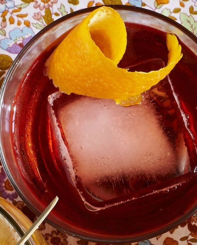bourbon negroni in a glass with a large square of ice and a curled strip of lemon peel