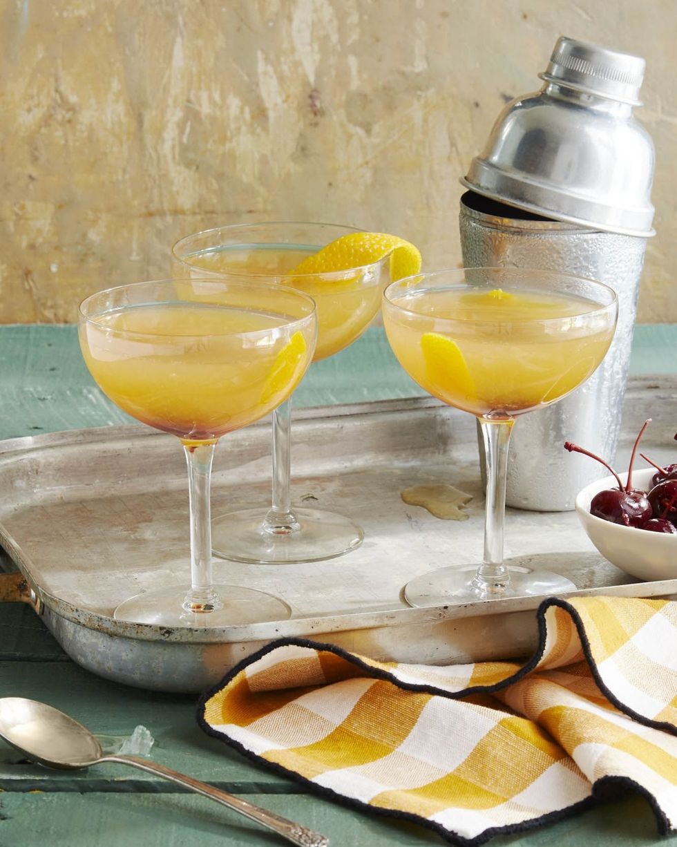 three cider sidecars in coupe glasses with strips of lemon peel as garnish