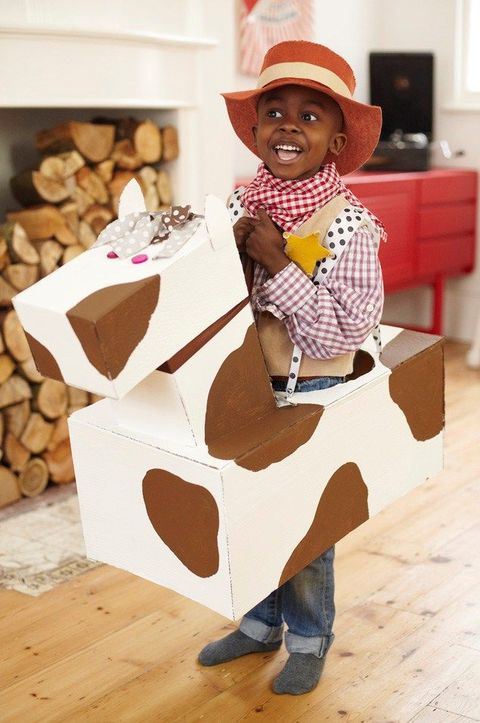 young boy wearing cowboy outfit and diy cow box costume that makes him look like he's riding a cow