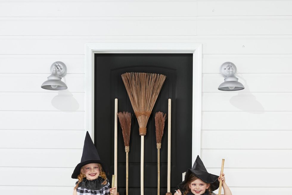 2 girls wearing halloween witch costumes with brooms, witch hats, and simple homemade black and white gingham dresses