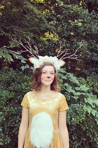 tween girl wearing deer halloween costume with flowered antlers headband and soft gold dress with white faux fur stomach