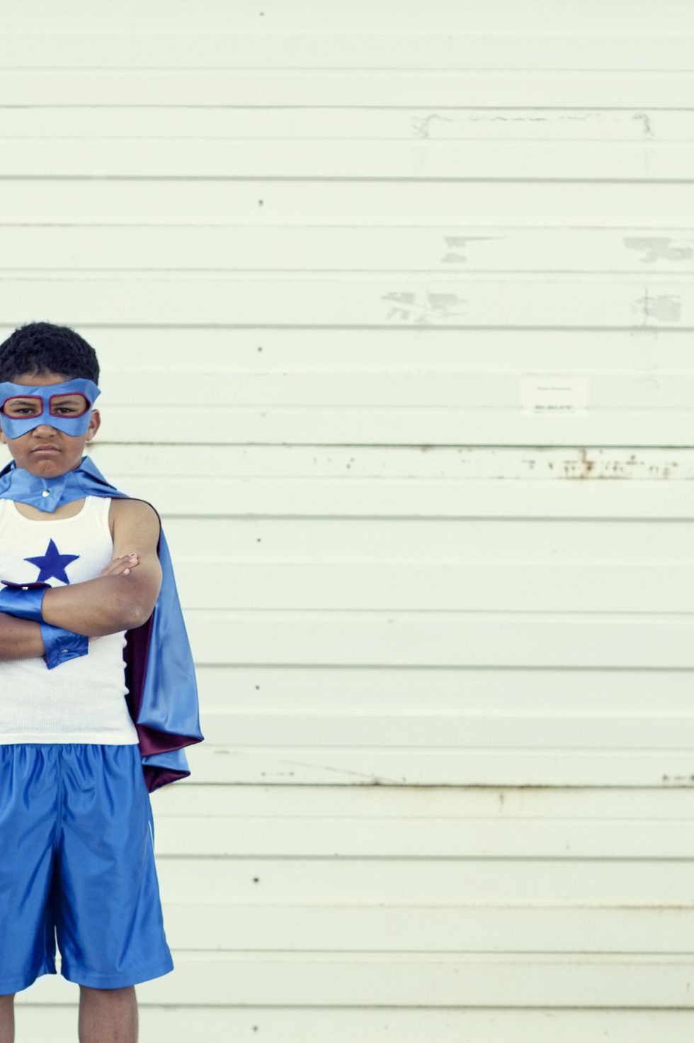 tween boy dressed as superhero halloween costume in blue mask, cape, and basketball shorts and tank with blue star on it