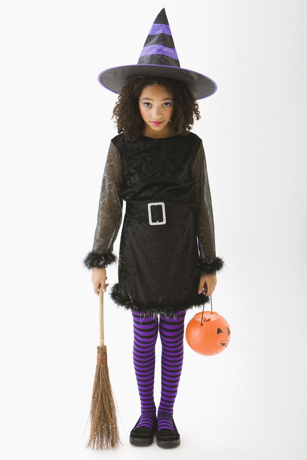 tween girl, 11 or 12 years old, in witch costume for halloween with hat, purple and black striped tights, belted black dress