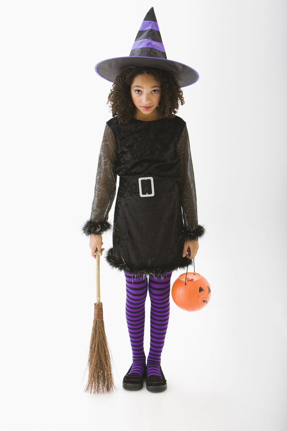 tween girl, 11 or 12 years old, in witch costume for halloween with hat, purple and black striped tights, belted black dress