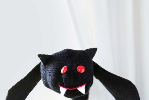 kids bat sock puppet crafted from black sock with black wings and ears, red button eyes and string mouth, and white fangs