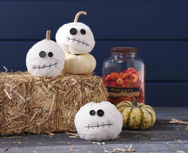 diy mummy pumpkins displayed on haystack with plain pumpkins and jar of old orange buttons