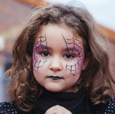 little girl with spider web painted on face looking at camera halloween