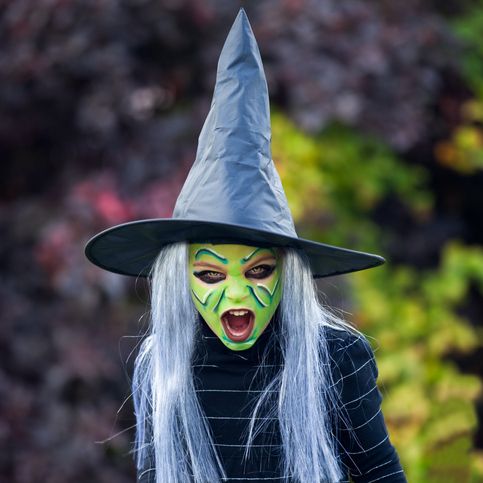 screaming little girl dressed up as witch complete with hat, gray wig and green face paint