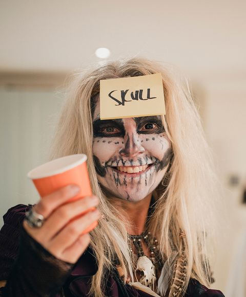 woman at halloween party wearing skeleton costume with sticky note on her forehead that says skull