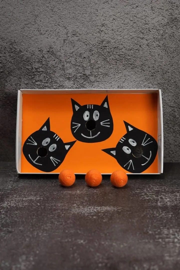 Three construction paper cats without noses and three balls that can be balanced to form noses