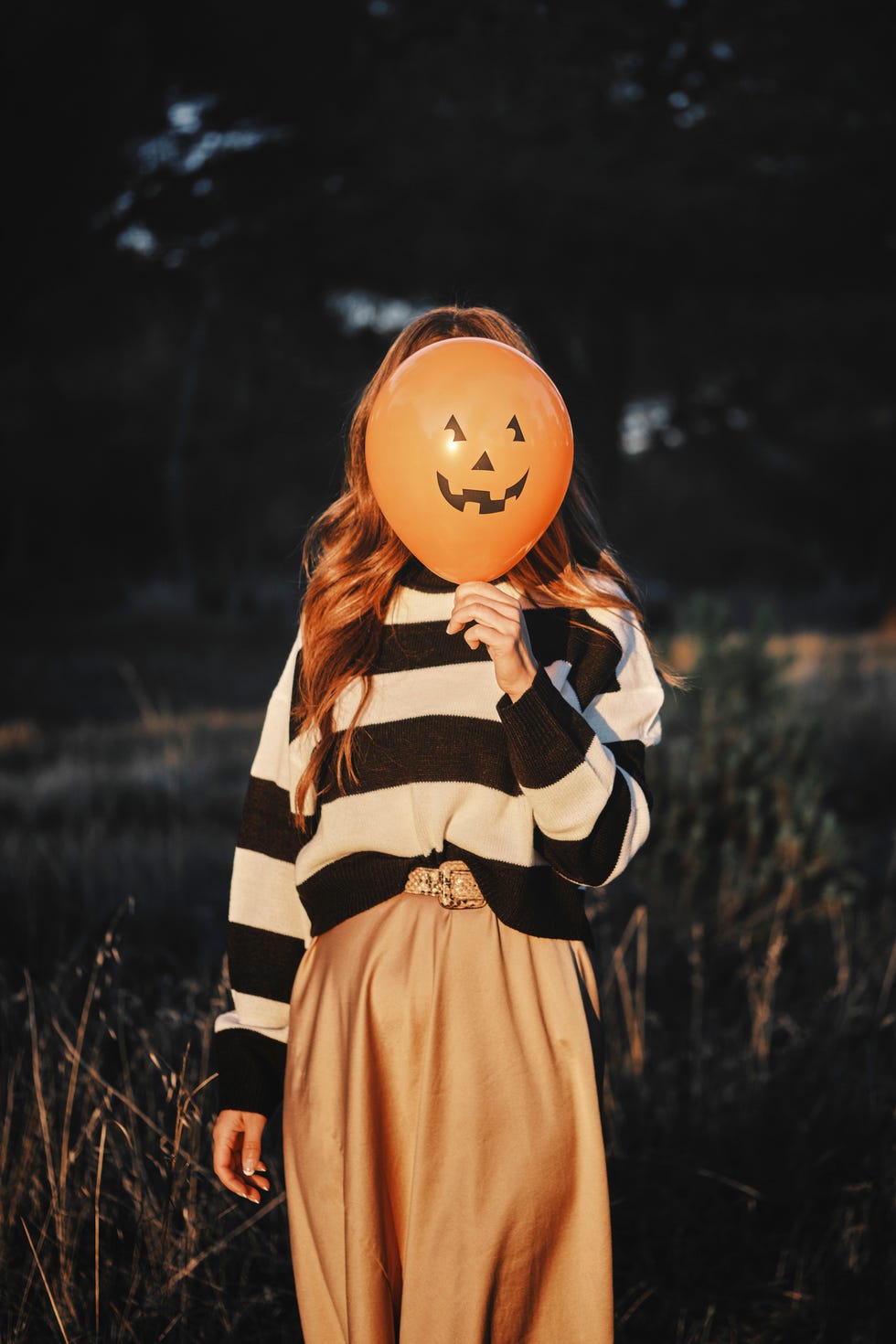 woman holding a pumpkin balloon in front of her face outdoors