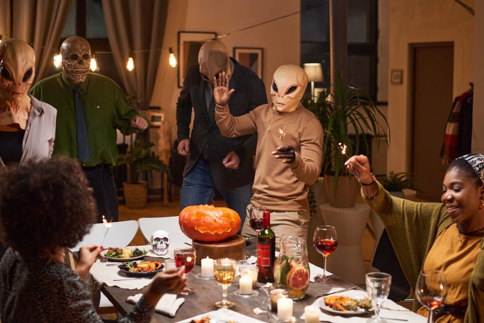 group of friends in costumes having fun at the table during halloween party in the room