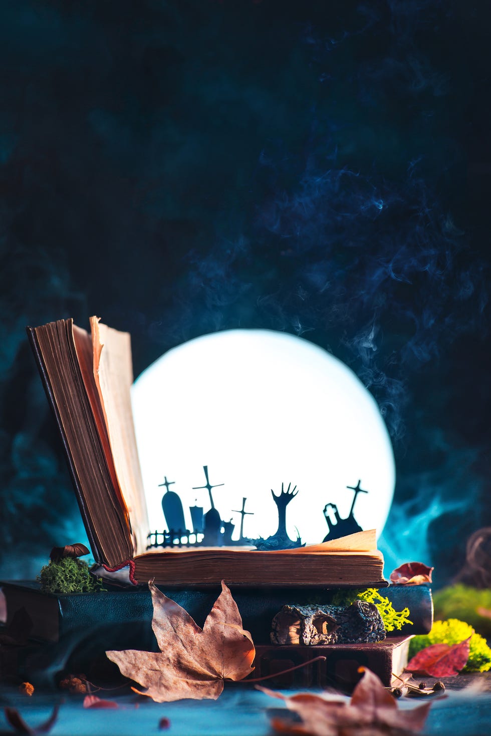 open book with silhouettes of graveyard and zombie hands