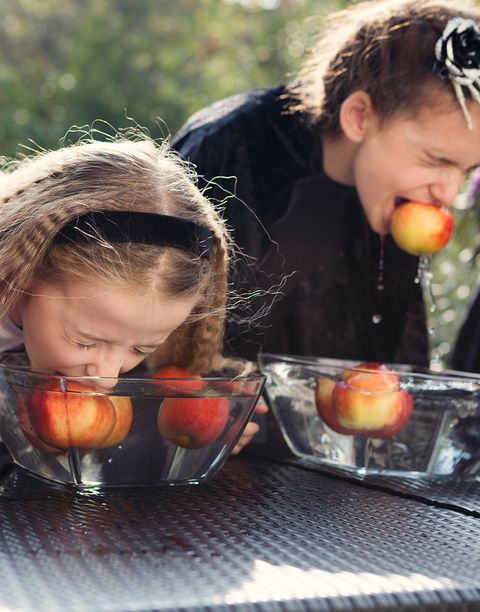 two young girls dressed in halloween costumes bobbing for apples at a halloween party