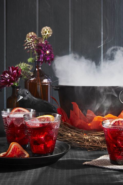 halloween punch pomegranate rum punch with orange garnish in glasses by a dutch oven cauldron smoking with dry ice