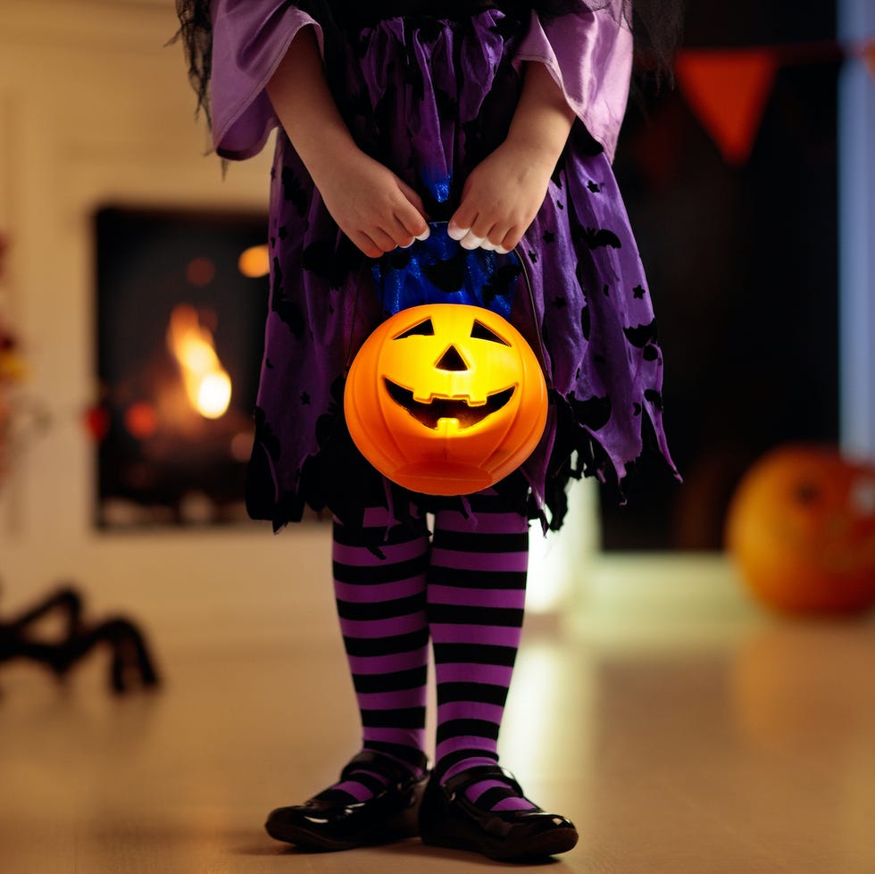 Kids in witch costume on Halloween trick or treat little girl in witch costume on halloween trick or treat at home pumpkin and candle decoration of fireplace dressed up child trick or treating kid holding candy bucket kids celebrate halloween