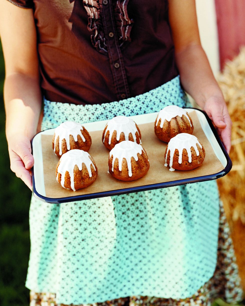 woman holding a white tray with black trim with six mini apple cardamom cakes with apple cider icing on it