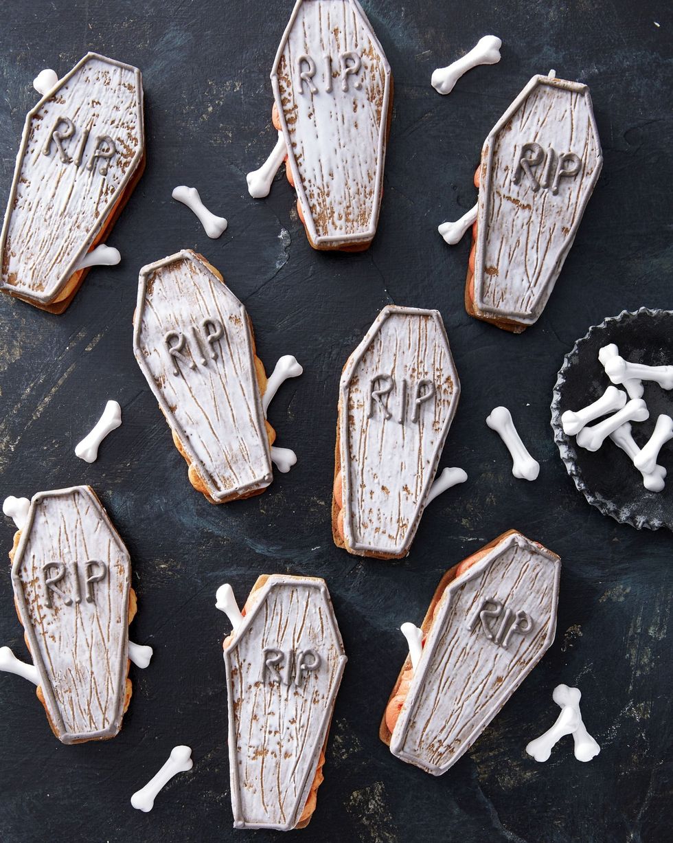 coffin sandwich cookies arranged on a black surface with a small bowl of bone shaped sprinkles