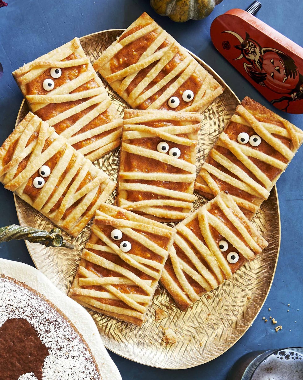 mummy pumpkin hand pies with google eye sprinkles arranged on a gold oval serving plate