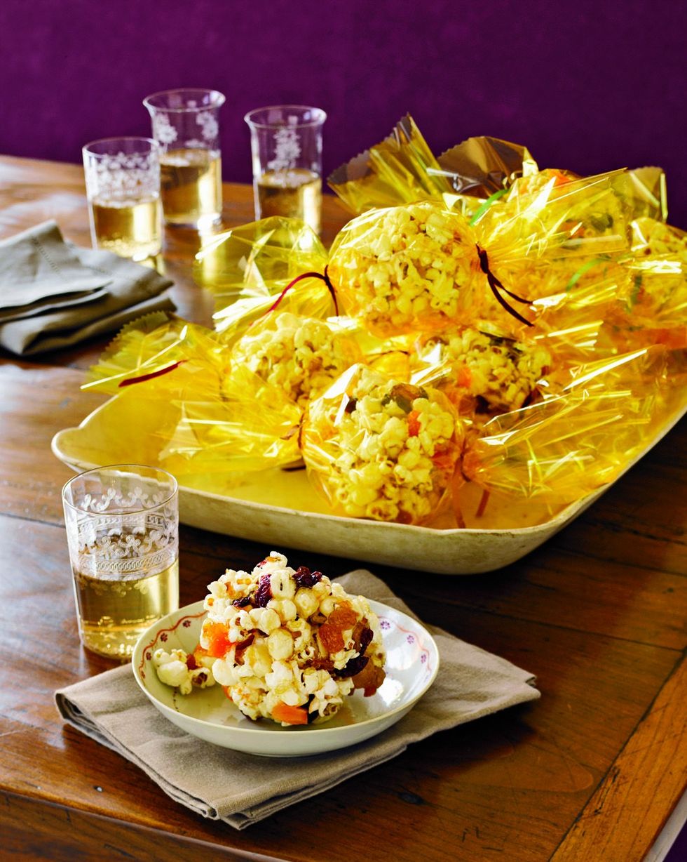 one sweet popcorn ball in a small bowl and more wrapped in yellow treat bags arranged in a serving tray
