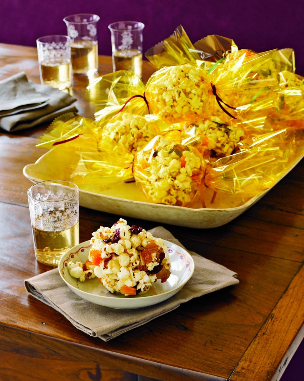 one sweet popcorn ball in a small bowl and more wrapped in yellow treat bags arranged in a serving tray