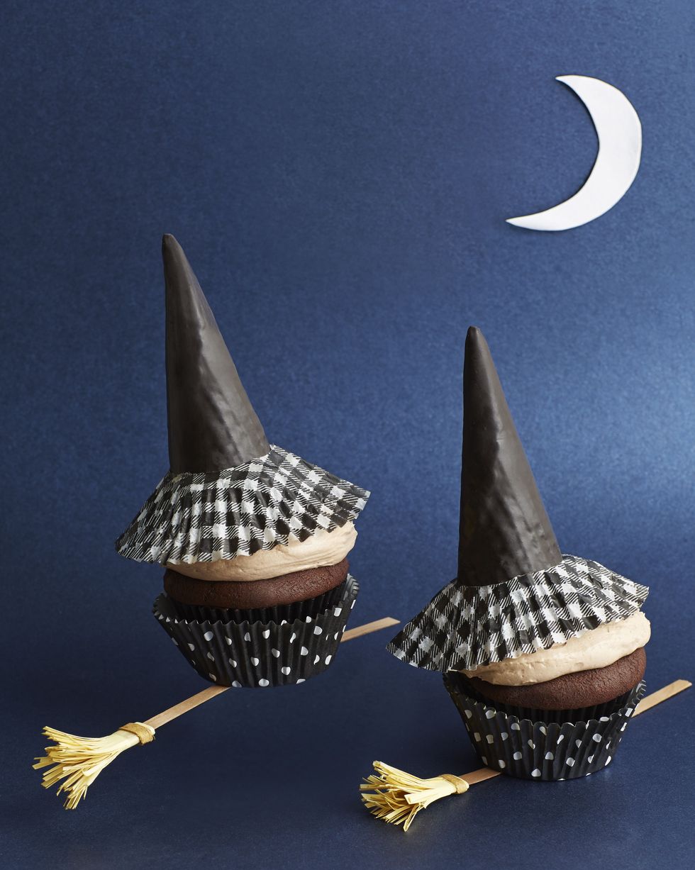 chocolate pumpkin cupcakes with witch hats on top made of ice cream cones and a small paper broom positioned underneath the cupcakes