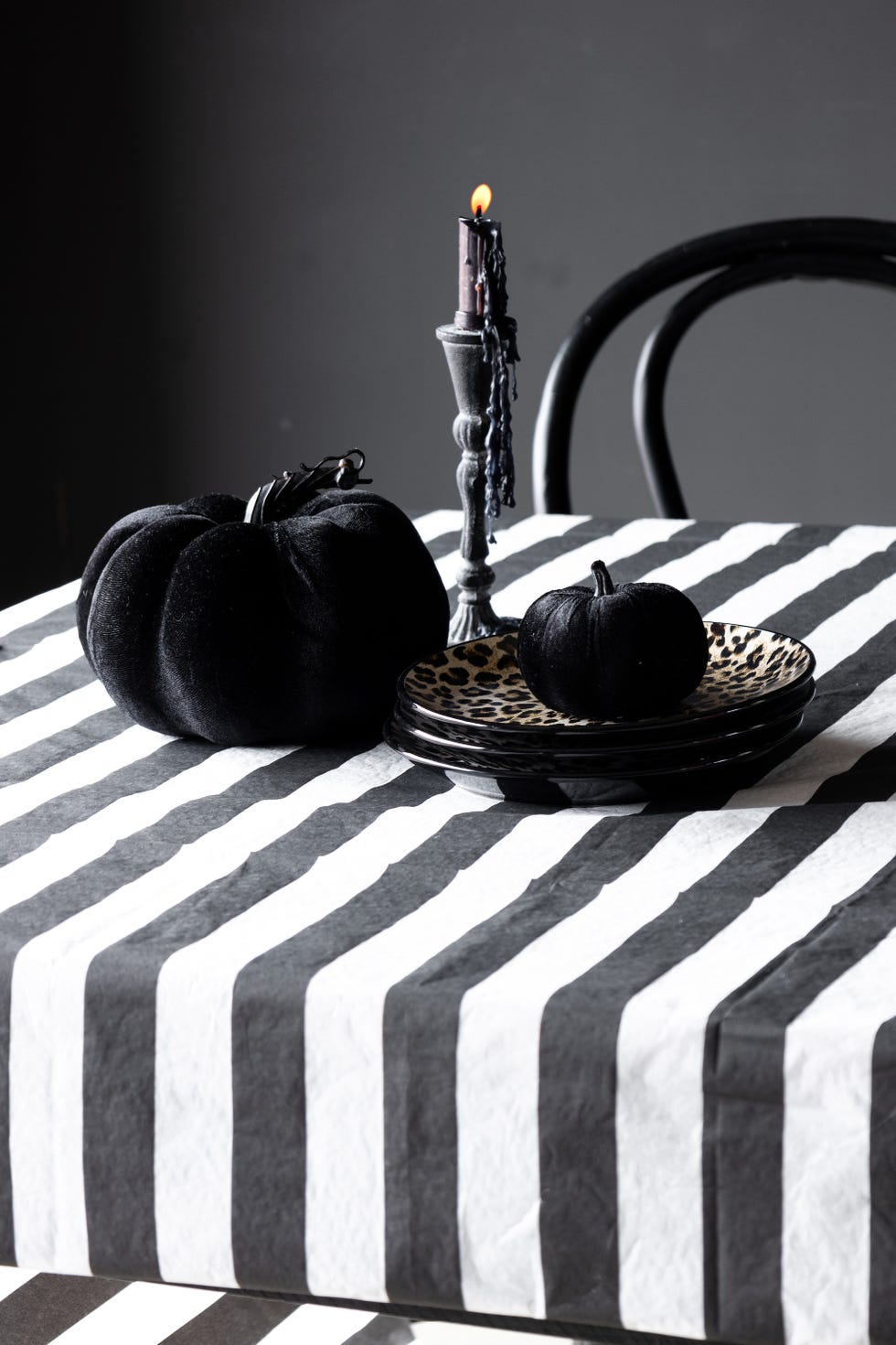 Two plush black pumpkins are displayed on a table adorned with a black and white striped tablecloth