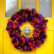 orange black and purple halloween wreath hanging on yellow door with skeleton