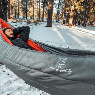 a person lying on a hammock with an underquilt in the snow