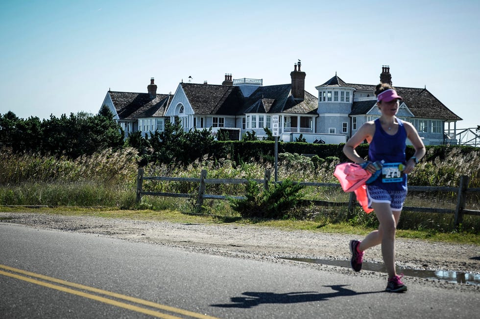 a woman running in a race with a large beachfront home in the background