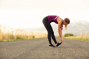 vrouw in sportkleding buigt voorover om hamstrings te rekken