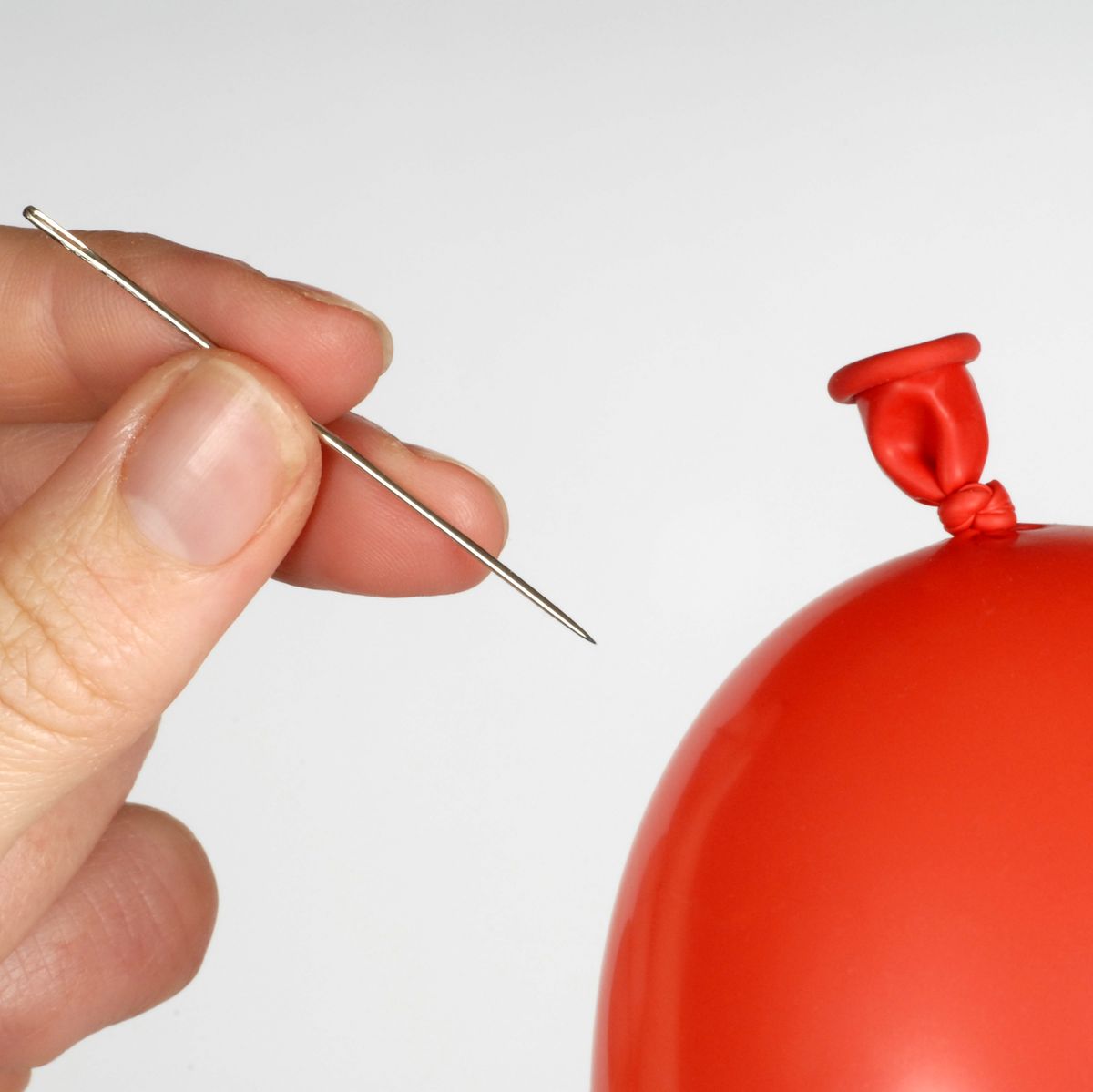 Hand holding a needle about to pop a red balloon