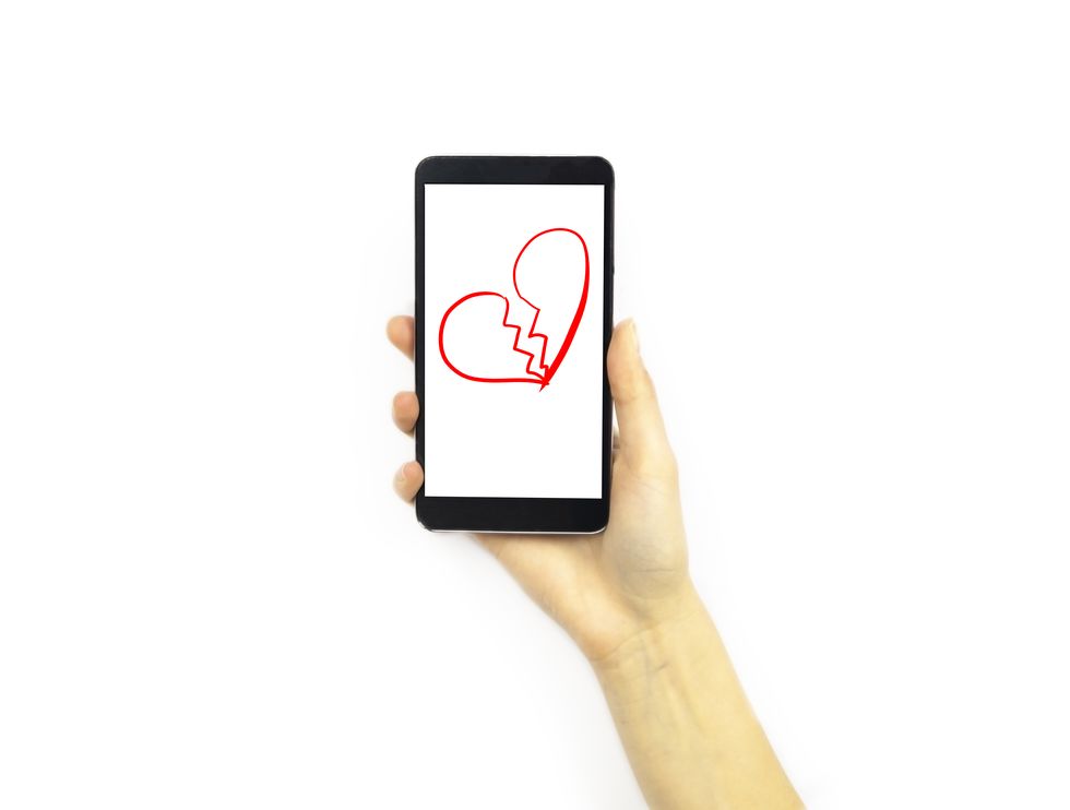 Hand holding a phone with a broken heart on it