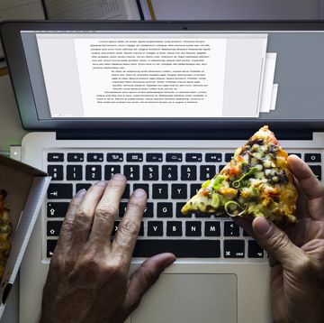 hand holding a pizza while working on a laptop