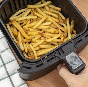 hand holding air fryer basket with freshly made french fries or fried potatoes in the kitchen. top view.