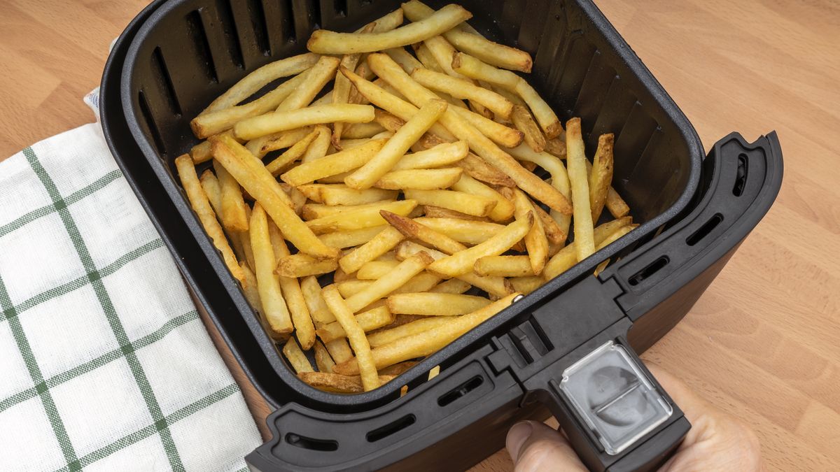 hand holding air fryer basket with freshly made french fries or fried potatoes in the kitchen. top view.