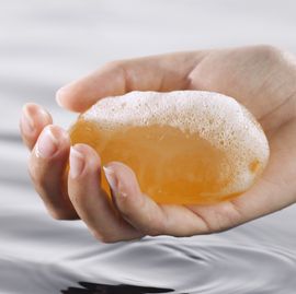 a hand holding a sudsy bar of kojic acid soap