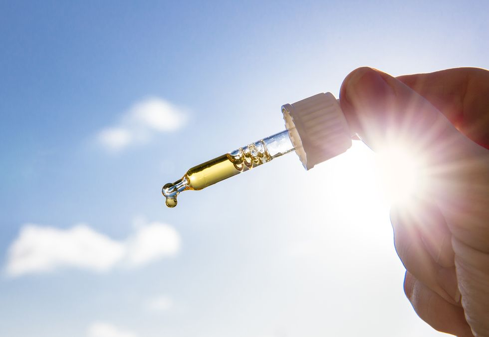 hand holding dropper pipette with nice golden liquid d vitamin against sun and blue sky on sunny day vitamin d keeps you healthy while lack of sun in winter, cure concept