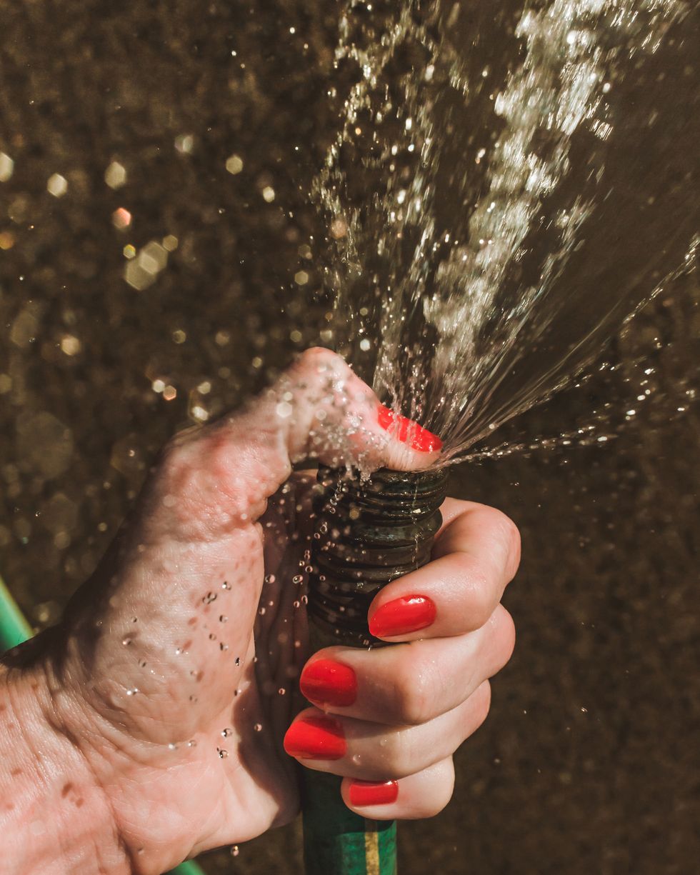 hand holding hose, running water outside, red nails, red nailpolish