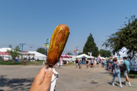 best state fair food every state hand holds up a pronto pup smothered in mustard at the fairgrounds in summer