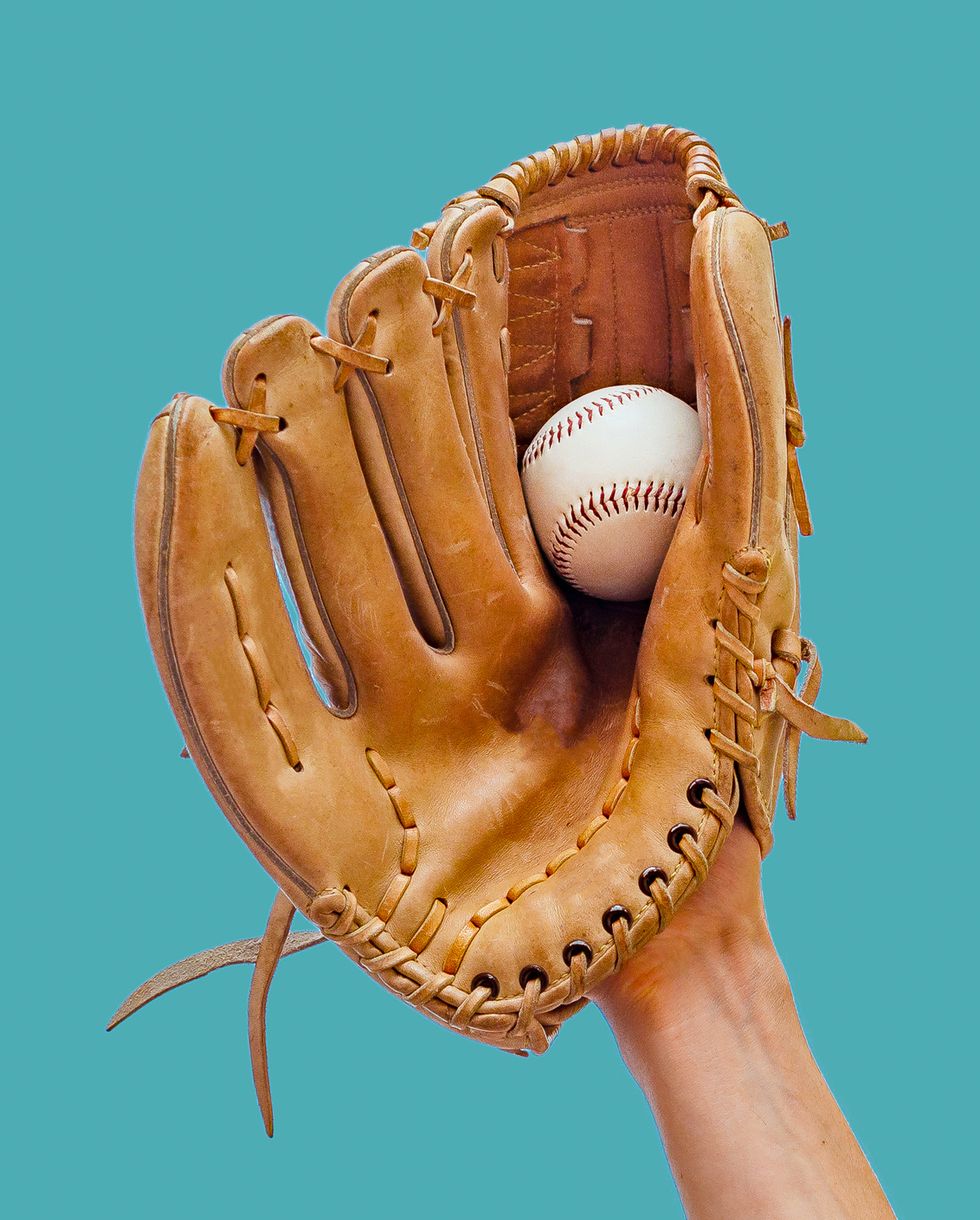 hand in a leather baseball glove catches a white ball in defocus on a red background