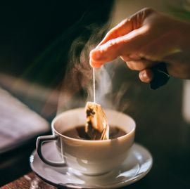 hand is picking a tea bag out of a white cup.