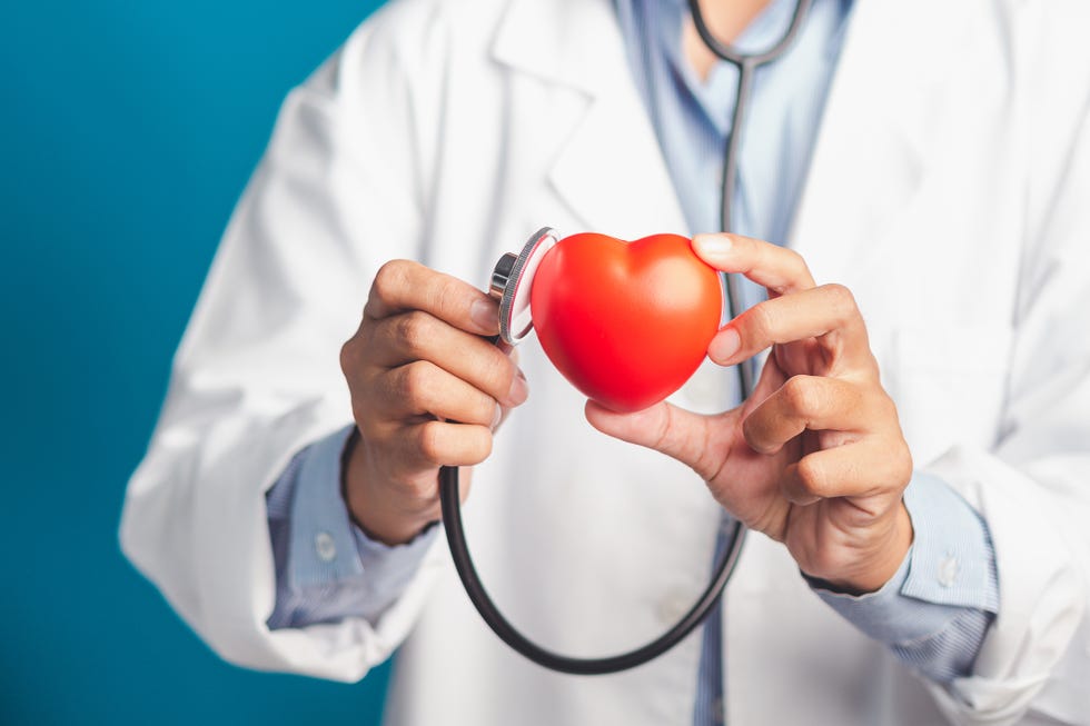 hand of a doctor holding a stethoscope checking a red heart shape while standing in the hospital or clinic