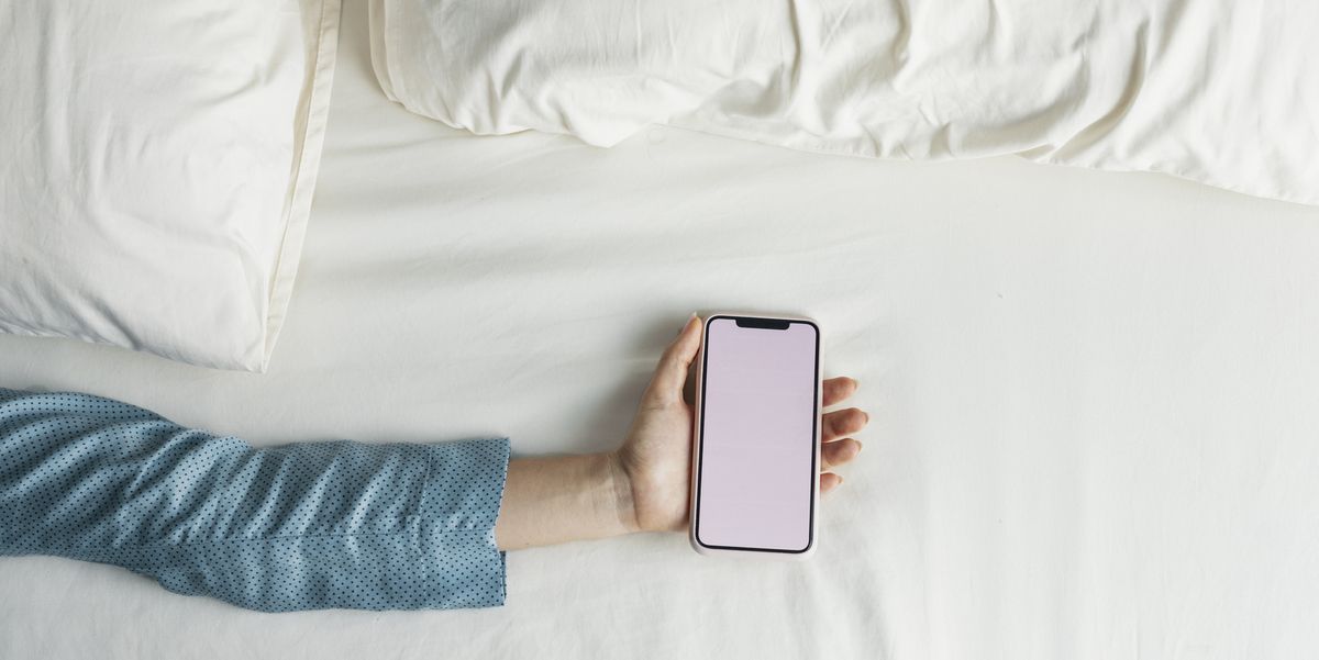 sleeping apps hand of a woman in pyjamas holding a smartphone on the bed