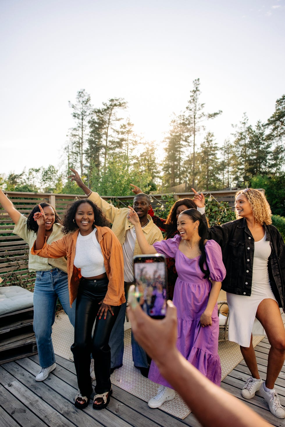 hand of man filming male and female friends dancing together in back yard