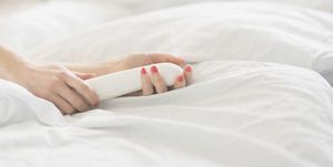 Hand of woman holding sex toy in bed