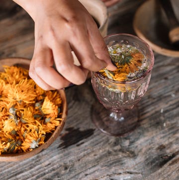 Hand of woman preparing fresh herbal tea with flower in glass on wooden table