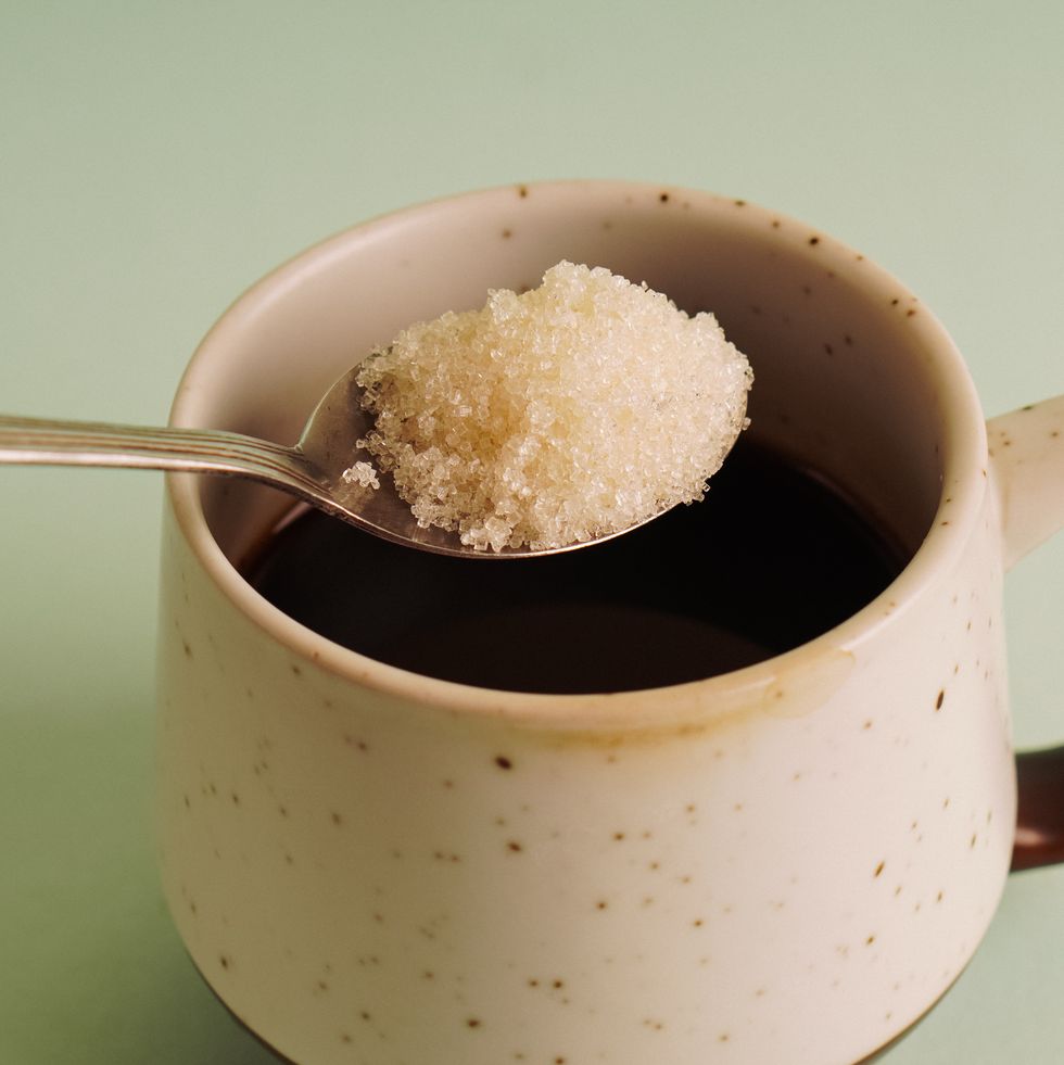 hand putting sugar on a cup of coffee against mint green background