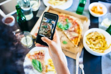 Hand taking cell phone picture of pizza on table
